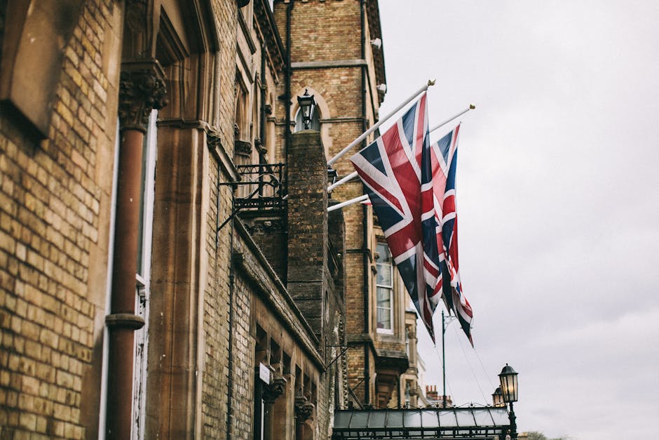 Union Jack flags adorning a historic brick building in Oxford, UK, on a cloudy day.