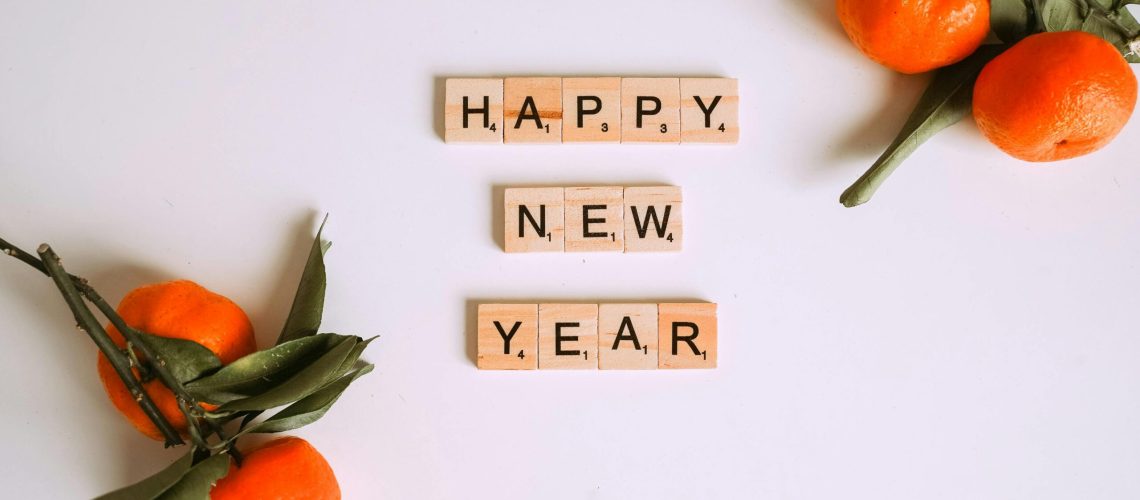 Happy New Year message with Scrabble tiles and fresh mandarins for festive decor.